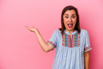 Middle age caucasian woman isolated on pink background impressed holding copy space on palm.