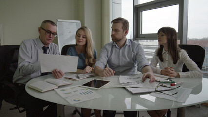 Colleagues at meeting in boardroom sitting at table together sharing ideas discussing strategy
