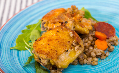 Baked chicken thighs with barley porridgeand begetables on striped tablecloth