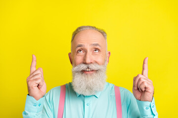 Photo of beaming old man point look up wear blue shirt isolated on vivid yellow color background