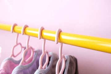 Set of several bodysuit hanging on clothes hangers hang on a yellow rack on a pink background