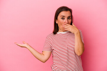 Middle age caucasian woman isolated on pink background impressed holding copy space on palm.