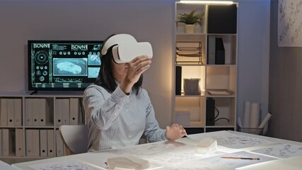 Tracking slowmo of female engineer in VR headset sitting at light table in office and working on project in virtual reality
