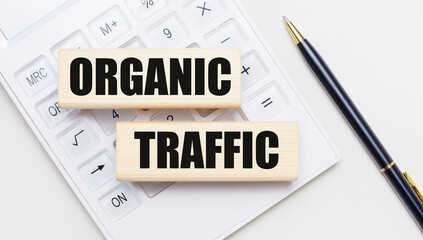 Wooden blocks with the text ORGANIC TRAFFIC lie on a light background on a white calculator. Nearby...
