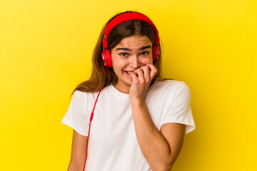 Young caucasian woman listening to music isolated on yellow background biting fingernails, nervous and very anxious.