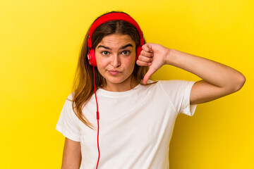 Young caucasian woman listening to music isolated on yellow background showing a dislike gesture, thumbs down. Disagreement concept.
