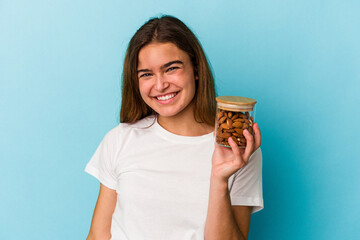 Young caucasian woman holding an almond jar isolated on blue background happy, smiling and cheerful.