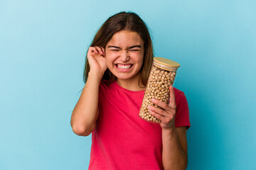 Young caucasian man holding chickpeas jar isolated on white background covering ears with hands.