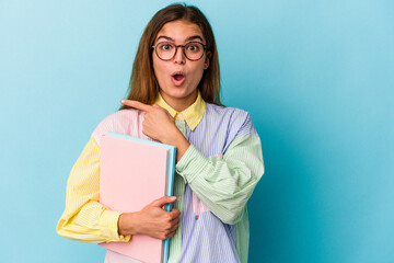 Fototapeta premium Young caucasian student woman holding books isolated on blue background pointing to the side