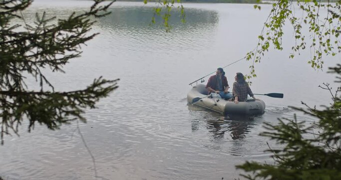 Young fishermen on an inflatable boat on the lake are fishing. Cinematic shot.