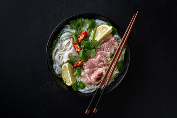 Pho Bo vietnamese soup with beef and rice noodles on a black background, top view - obrazy, fototapety, plakaty