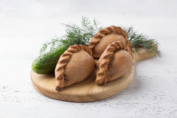 Russian traditional rye pies with egg, kokurki, on light gray background with cucumber and herbs. Delicious homemade food and snack