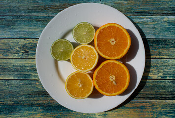 fruits - oranges, lemons, limes lie on a white plate on a blue background. citrus fruit