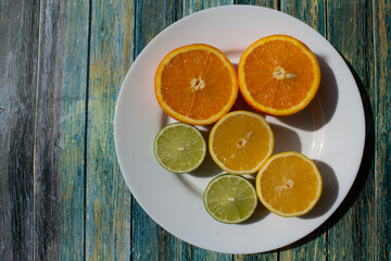 fruits - oranges, lemons, limes lie on a white plate on a blue background. citrus fruit