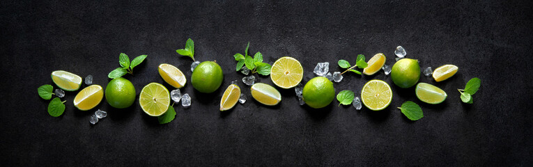 Fresh limes with ice cubes and mint leaves on dark wet panoramic background