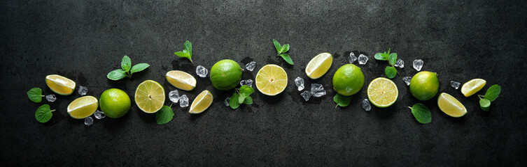 Fresh limes with ice cubes and mint leaves on dark wet panoramic background