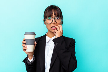 Young business mixed race woman holding a coffee isolated on blue background biting fingernails,...