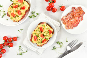 Scrambled eggs with microgreen, bacon and tomatoes on bread