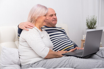 handsome senior couple woman and man sitting in bed using laptop at home.