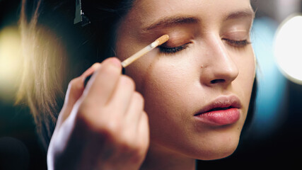 Obraz premium makeup artist applying concealer on eyelid of young woman