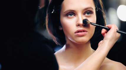makeup artist applying face powder on face of model