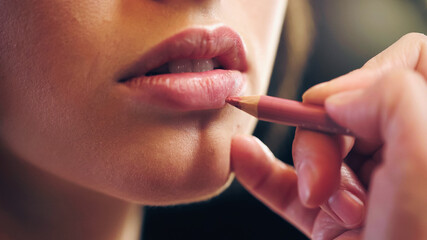 cropped view of makeup artist applying lip pencil on lips of young woman