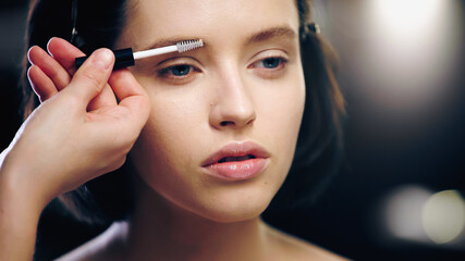 makeup artist brushing eyebrow of young model