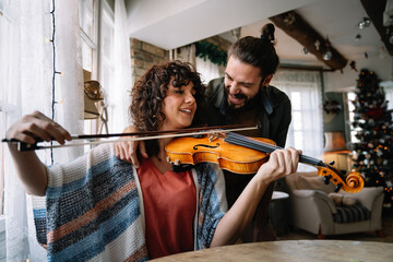 Private male music teacher giving violin lessons to a woman at home