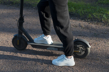 Young woman stands on a kick scooter in white sneakers and black pants in the profile