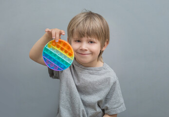 Fototapeta na wymiar the boy is holding a silicone antistress pop it toy with a round shape and rainbow color