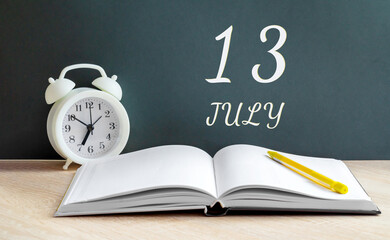 july 13. 13-th day of the month, calendar date.A white alarm clock, an open notebook with blank pages, and a yellow pencil lie on the table.Summer month, day of the year concept