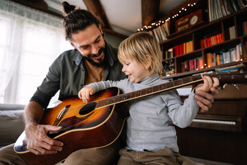 Cute little boy and his handsome father are playing guitar and smiling at home