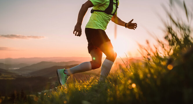 Cropped photo of Middle-aged mountain trail runner man dressed bright t-shirt with a backpack endurance running uphill by picturesque hills at sunset time. Sporty active people concept image.
