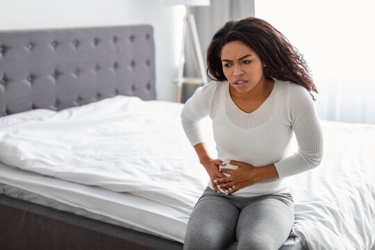 Woman With Right Side Pain Sitting On Bed At Home