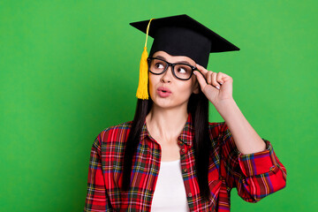 Portrait of attractive minded girl wearing master's cap touching specs copy space isolated over bright green color background