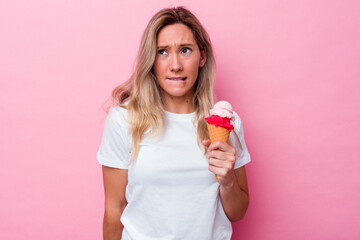 Young australian woman holding an ice cream isolated on pink background confused, feels doubtful and unsure.