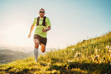 Active mountain trail runner dressed bright t-shirt with a backpack in sports sunglasses running...