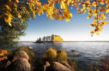 Beautiful sunny autumn island in frame of golden leaves and stones. Fall in Vyborg bay, gulf of Finland