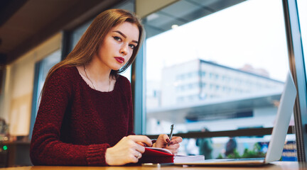 Thoughtful woman taking notes in notebook