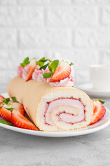 Cake roll with fresh strawberries, jam and cream cheese on a white plate on a gray background. Copy space.