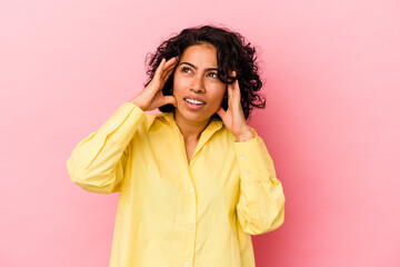 Young curly latin woman isolated on pink background covering ears with fingers, stressed and desperate by a loudly ambient.