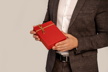 partial view of man in suit holding red gift box isolated on grey with lilac shade