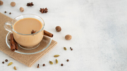 Masala tea chai in a glass cup with ingredients for cooking. Cinnamon sticks, ginger, cardamom, anise, honey, cloves. Traditional Indian drink - spicy black tea with spices and milk. Copy space.