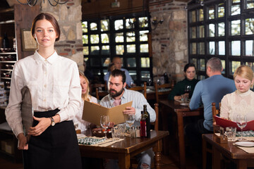 Positive woman waiter demonstrating country restaurant to visitors. High quality photo