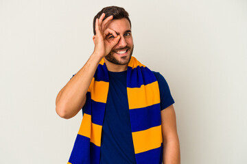 Young caucasian fan of a soccer team isolated on white background excited keeping ok gesture on eye.