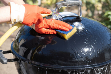 Male hand with gloves wash round grill with sponge and water hose. preparation of a grill before...