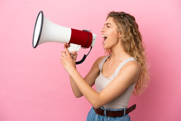 Young blonde woman isolated on pink background shouting through a megaphone to announce something...