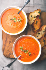 Tomato soup served with croutons and herbs
 in a white bowl on the olive wooden  tray and gray cotton background. Healthy food concept. Top view.