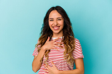 Young mexican woman isolated on blue background laughs happily and has fun keeping hands on stomach.