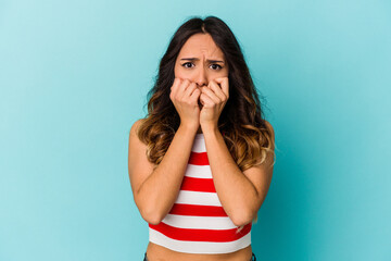 Young mexican woman isolated on blue background biting fingernails, nervous and very anxious.